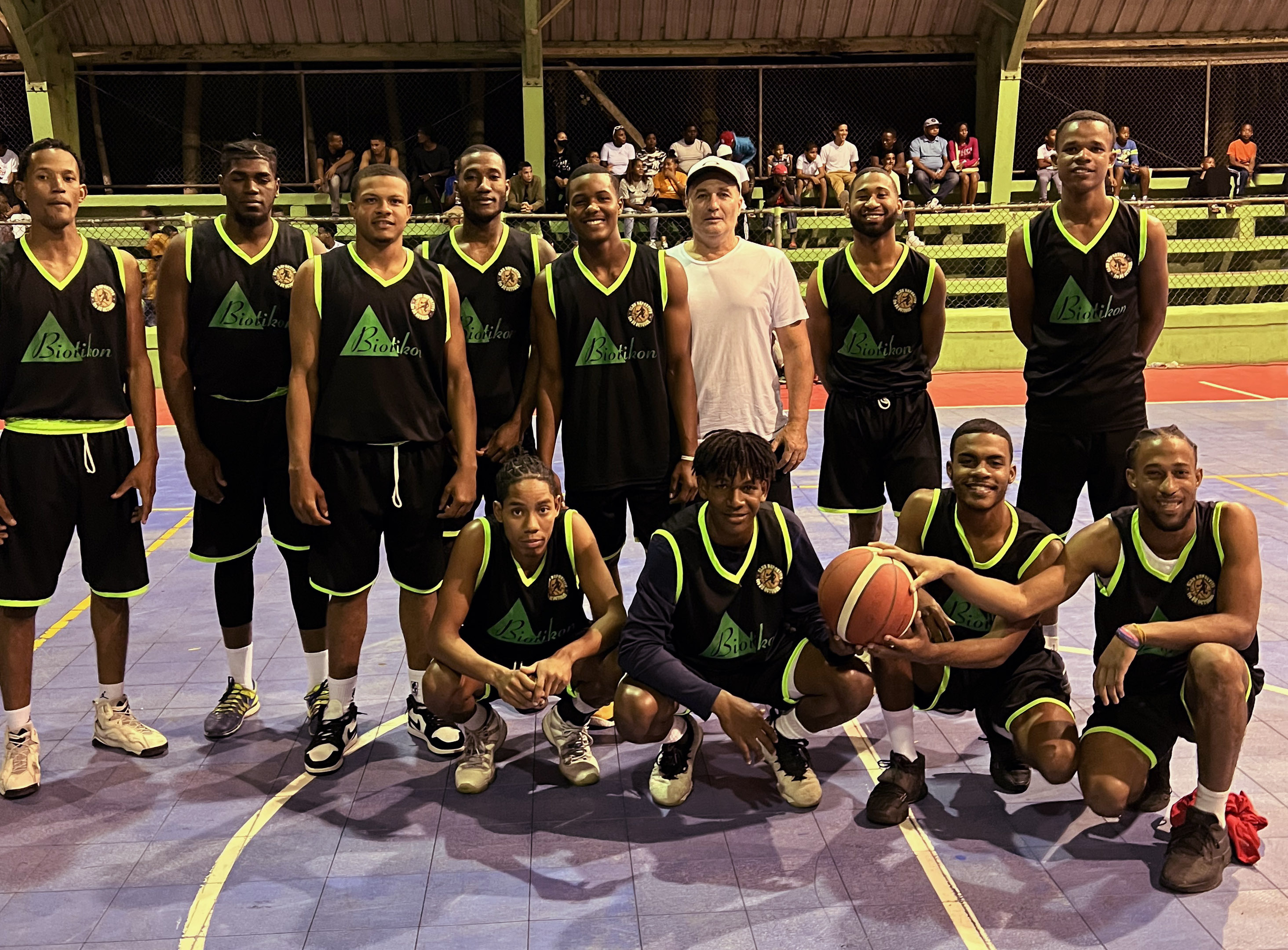 Basketball-Team – Gruppenfoto Eine Gruppe von Basketballspielern in schwarzen Trikots mit grünen Akzenten, auf dem Spielfeld stehend, mit Basketball und jubelnder Pose.