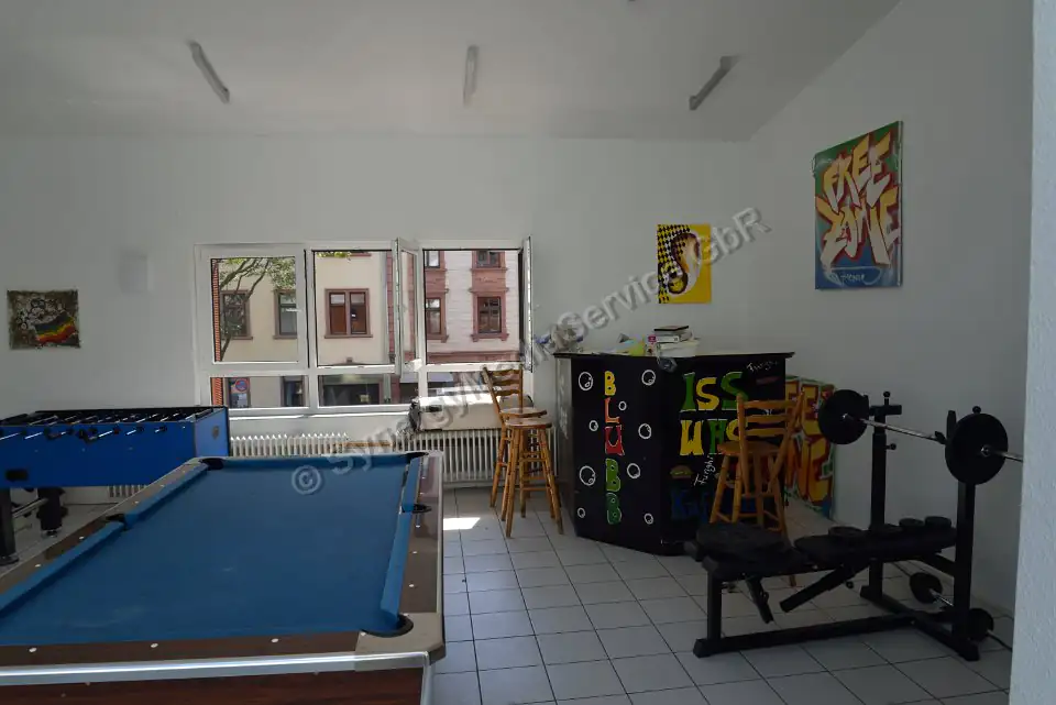 Freizeitraum mit Billardtisch und Fitnessgeräten Heller Freizeitraum mit Billardtisch, Tischfußball, Fitnessgerät und Bar, großer Fensterfront.